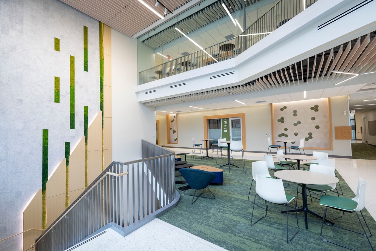 The lobby of an academic building shows chairs, tables and a second floor visible through glass.
