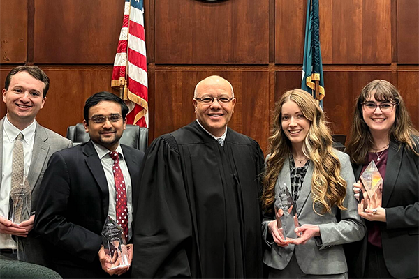 Five people pose for a photo in a courtroom while holding trophies.