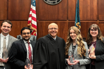 Five people pose for a photo in a courtroom while holding trophies.