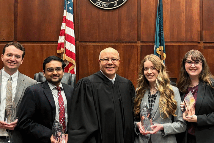 Five people pose for a photo in a courtroom while holding trophies.