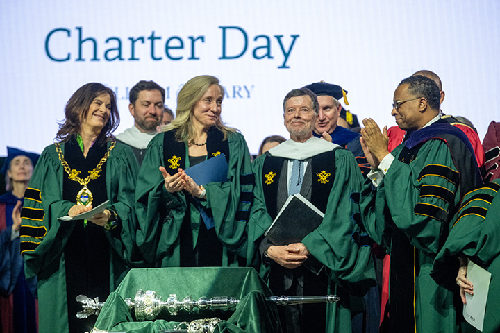 People wearing academic regalia applaud.