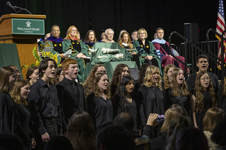 A choir sings while its members stand in front of a stage.