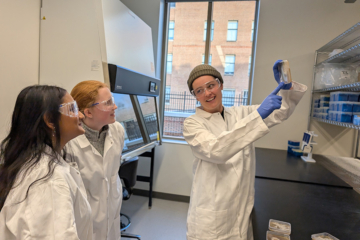 Three people stand in a lab and look at a culture.