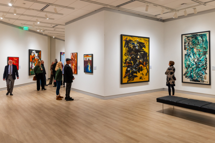 People walk around an art gallery with abstractionist art on the walls.