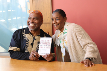 Two people pose for a photo together while one holds a book with the title "Black on Black."