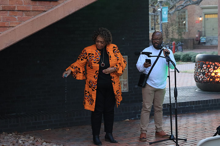 A person talks into a microphone while another person pours water onto the ground.