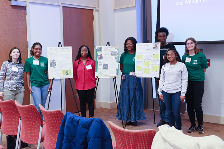 People wearing name tags stand near three posters on easels.