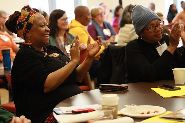 People sit at tables and clap during a Lemon Project symposium