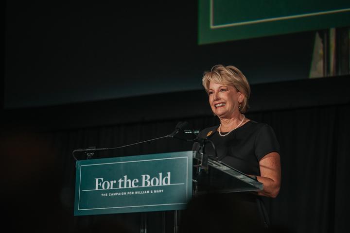 Sue Gerdelman stands at a podium with a "For the Bold" sign on the front of it.