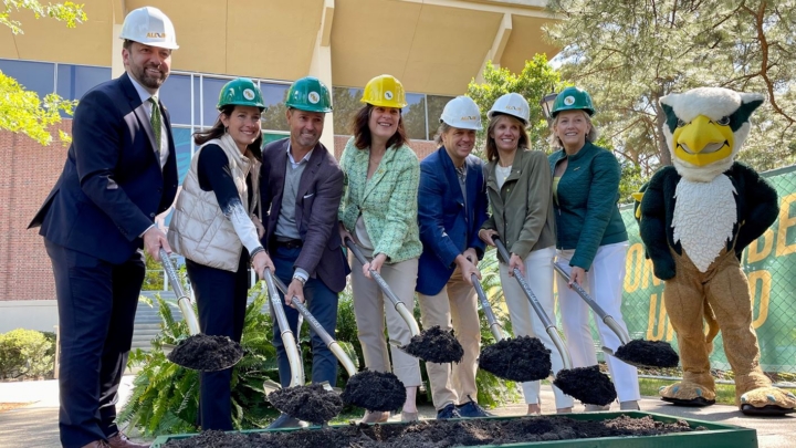 People wearing construction helmets and holding shovels lift up piles of dirt.
