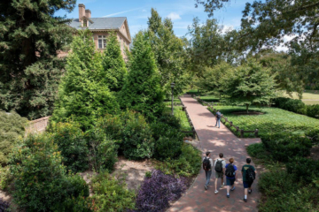 People with backpacks walk along a brick pathway toward a brick building.