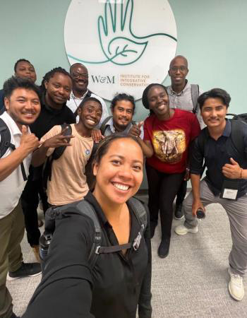 People take a selfie together in front of a wall with the logo for the Institute for Integrative Conservation.