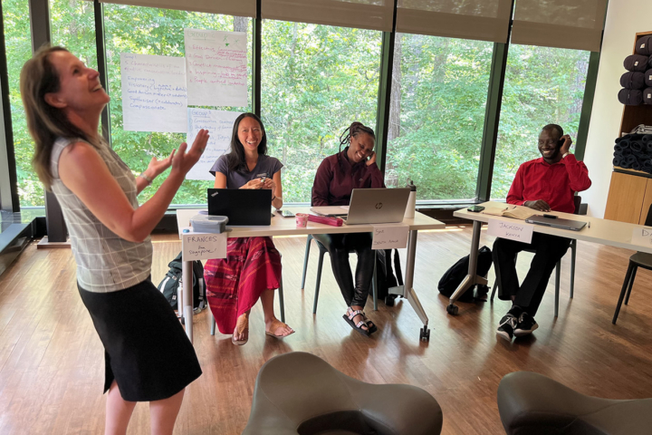 A person laughs while standing in a room near people sitting at tables with laptops.