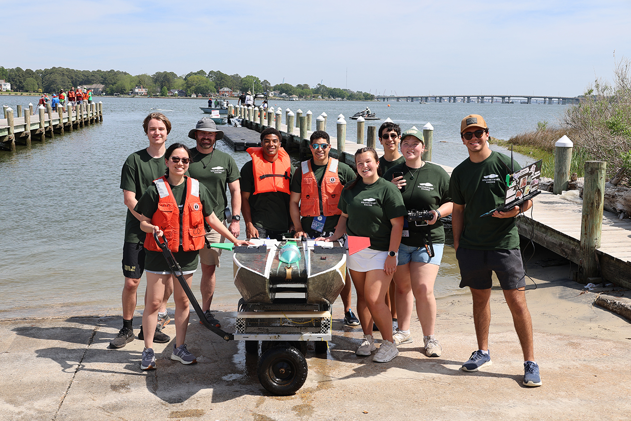 People wearing T-shirts and life vests stand by a boat near a dock.