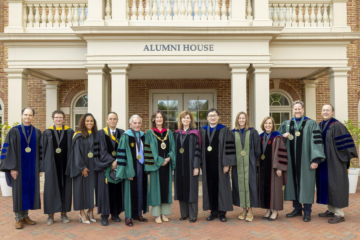 People wearing academic regalia take a photo together outside of the W&M Alumni House.
