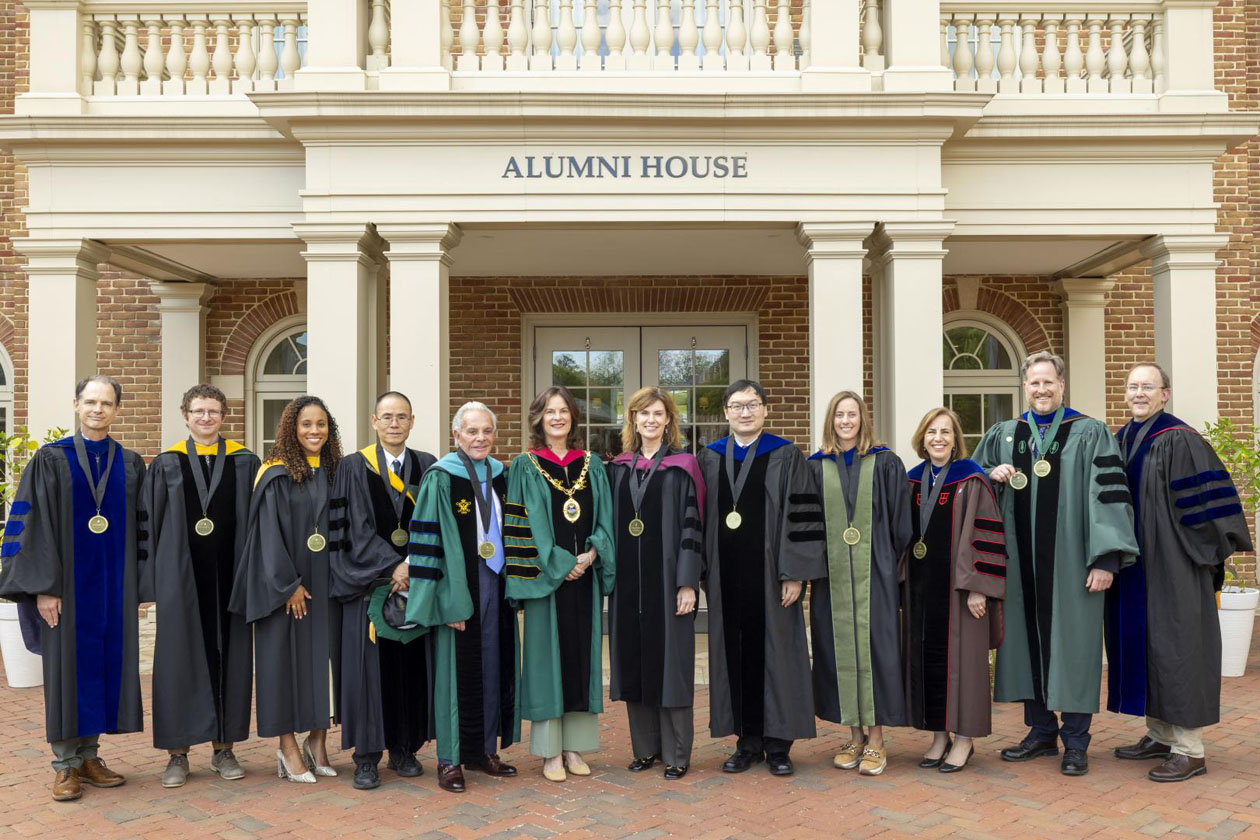 People wearing academic regalia take a photo together outside of the W&M Alumni House.