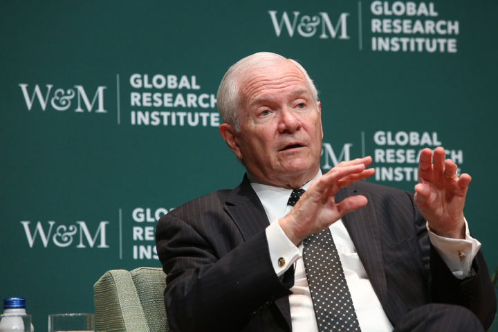 Robert Gates gestures while speaking in front of a backdrop that says W&M and Global Research Institute.