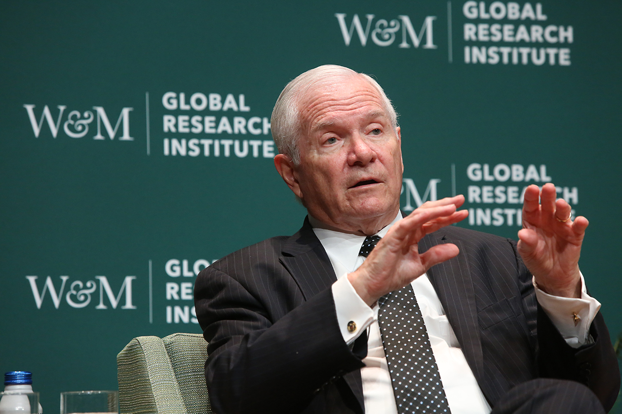 Robert Gates gestures while speaking in front of a backdrop that says W&M and Global Research Institute.