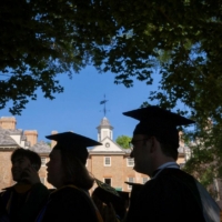 People in caps and gown are seen in silhouette against the Wren Building.