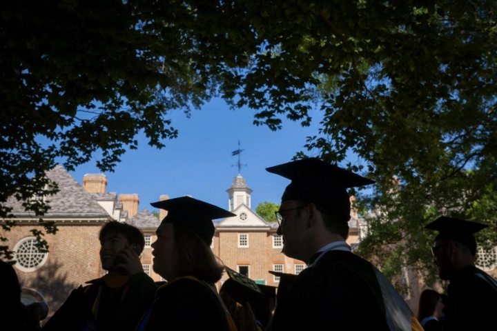 People in caps and gown are seen in silhouette against the Wren Building.