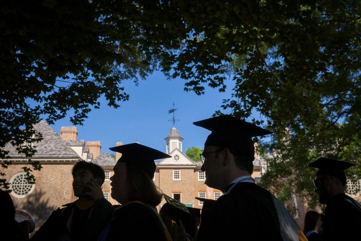 People in caps and gown are seen in silhouette against the Wren Building.