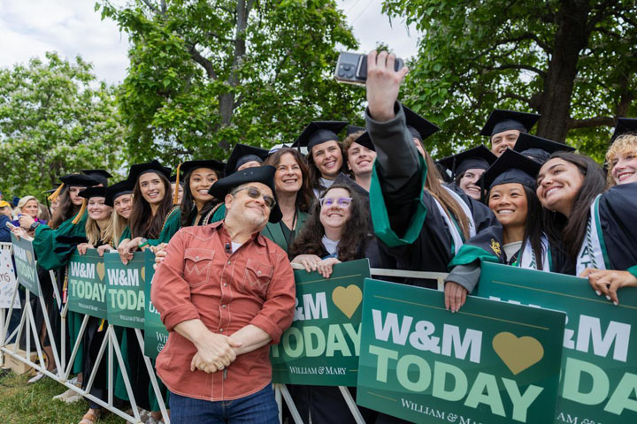 People in caps and gowns take a selfie with a celebrity.