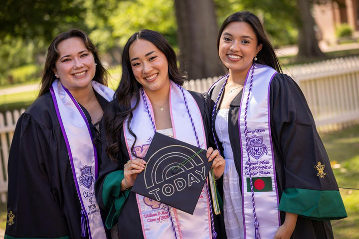 Three people in academic gowns smile for a photo together.