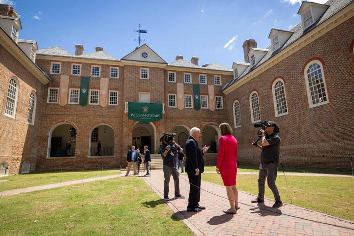 Two people hold news cameras and film two people standing outside of the Wren Building.
