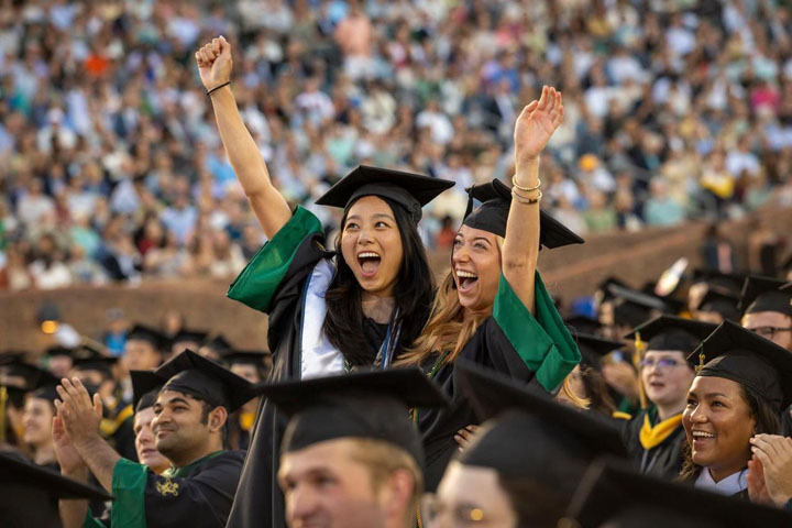 Two people in caps and gowns cheer and raise their arms.