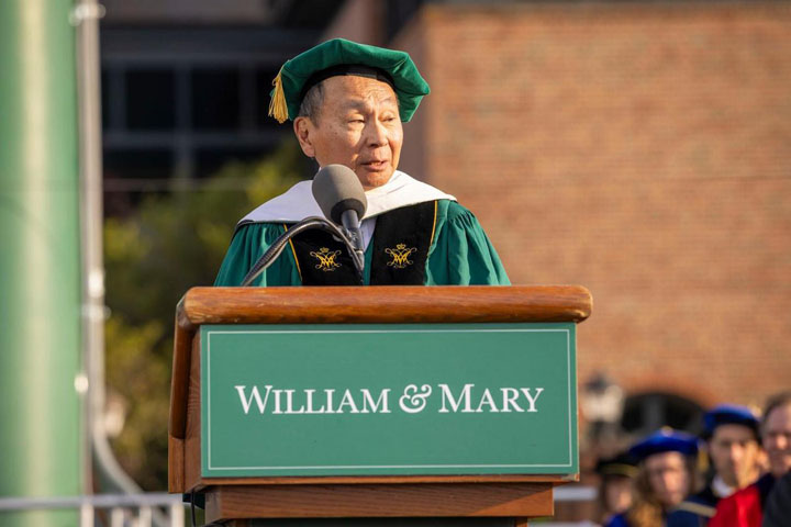 Francis Fukuyama wears a cap and gown and stands at a podium.