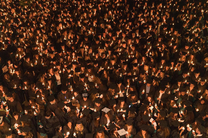 An aerial photo shows dozens of people in caps and gowns holding candles.