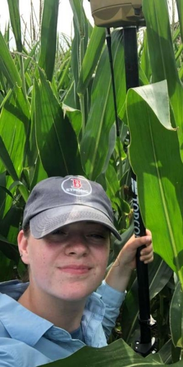 A person standing in a corn field holds a pole.