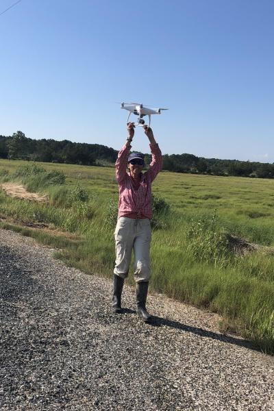 A person holds a drone over their head in a field.