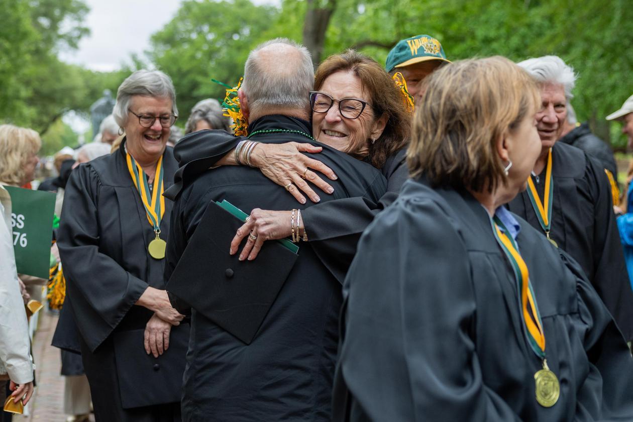 Two people embrace while standing among others.
