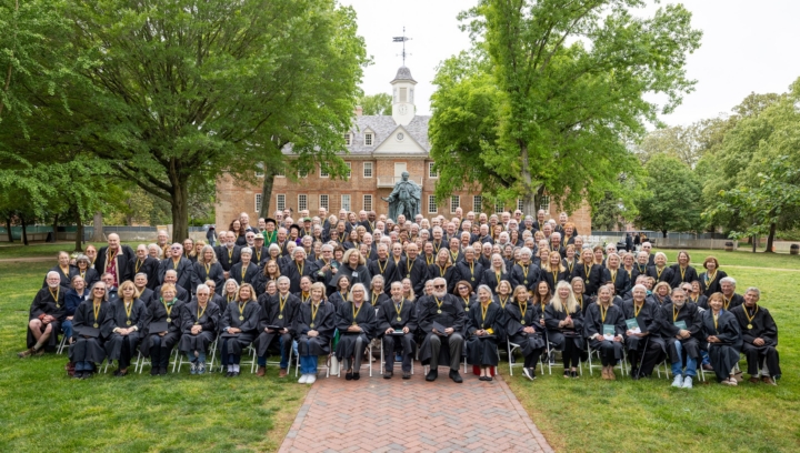 People in caps and gowns pose for a photo in front of the Wren Building.