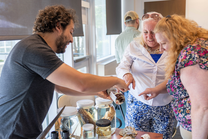 A person holds a jar up with a marine specimen inside of it while two people point.