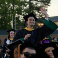 A graduate in a cap and gown waves.