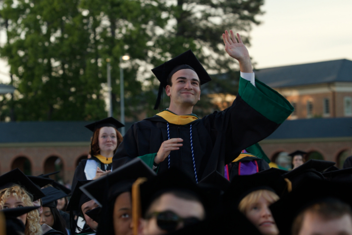 A graduate in a cap and gown waves.