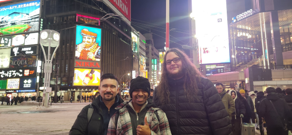 Three people pose for a photo together in a large city.