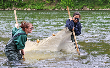 Two people hold a net between them while standing in a river.