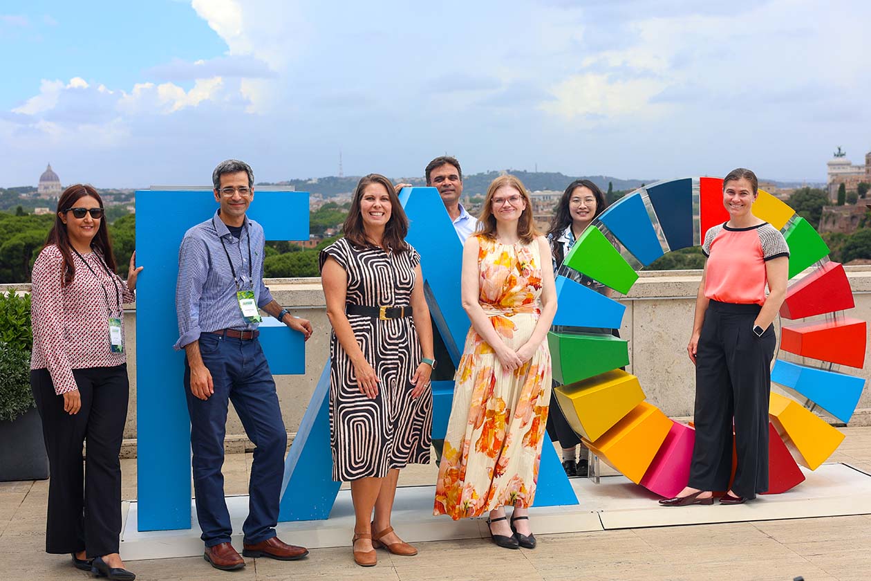 People pose for a photo together next to large FAO letters, overlooking a large body of water.