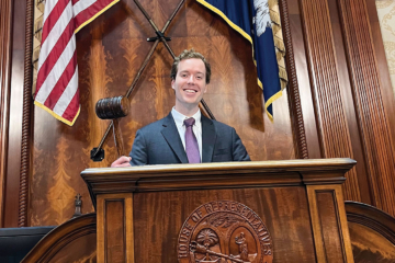 A person holds a gavel while standing at a wooden podium.
