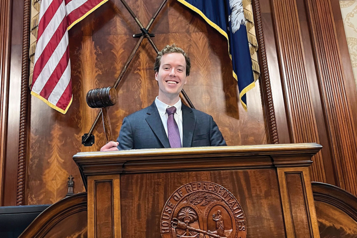 A person holds a gavel while standing at a wooden podium.