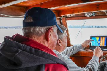 Two people look out from the bridge of a boat.