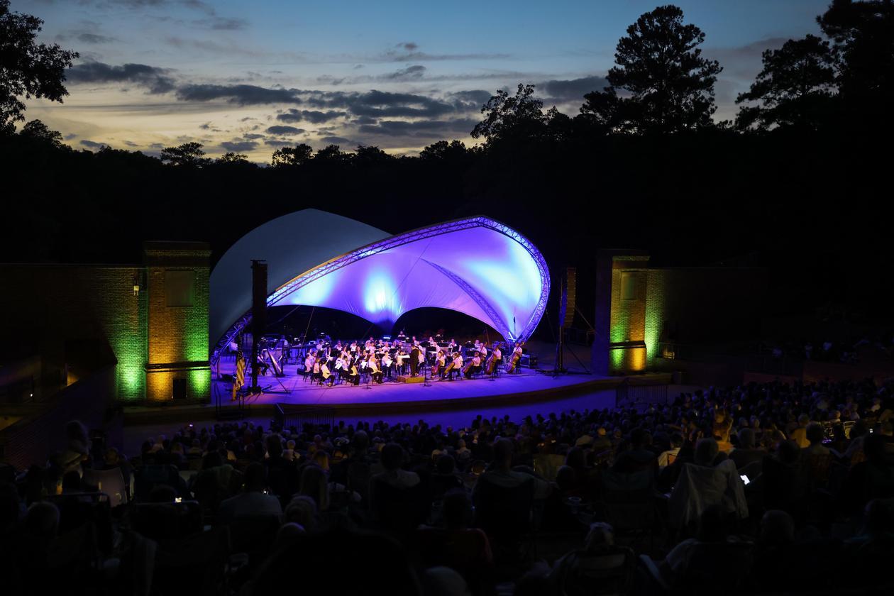 This is a photograph of the Virginia Symphony Orchestra performing on a summer night at the Martha Wren Briggs Amphitheatre at Lake Matoaka