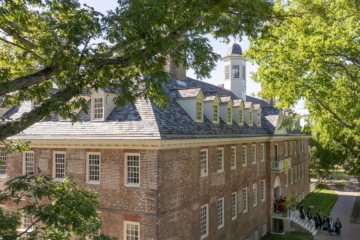 An aerial view of the Wren Building shows graduates streaming out of the front doors into a grassy area.