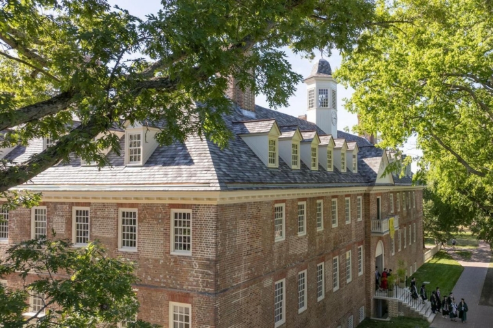 An aerial view of the Wren Building shows graduates streaming out of the front doors into a grassy area.
