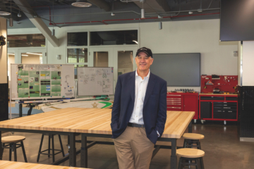 Bob Wise stands in front of a table in a large room.