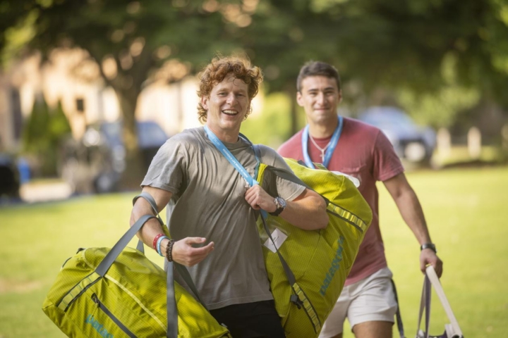 This is.a photo of two young men carrying big duffel bags on move in day for the class of 2030