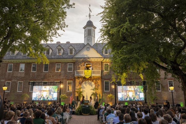 People sit in front of the Wren Building as the sun sets.